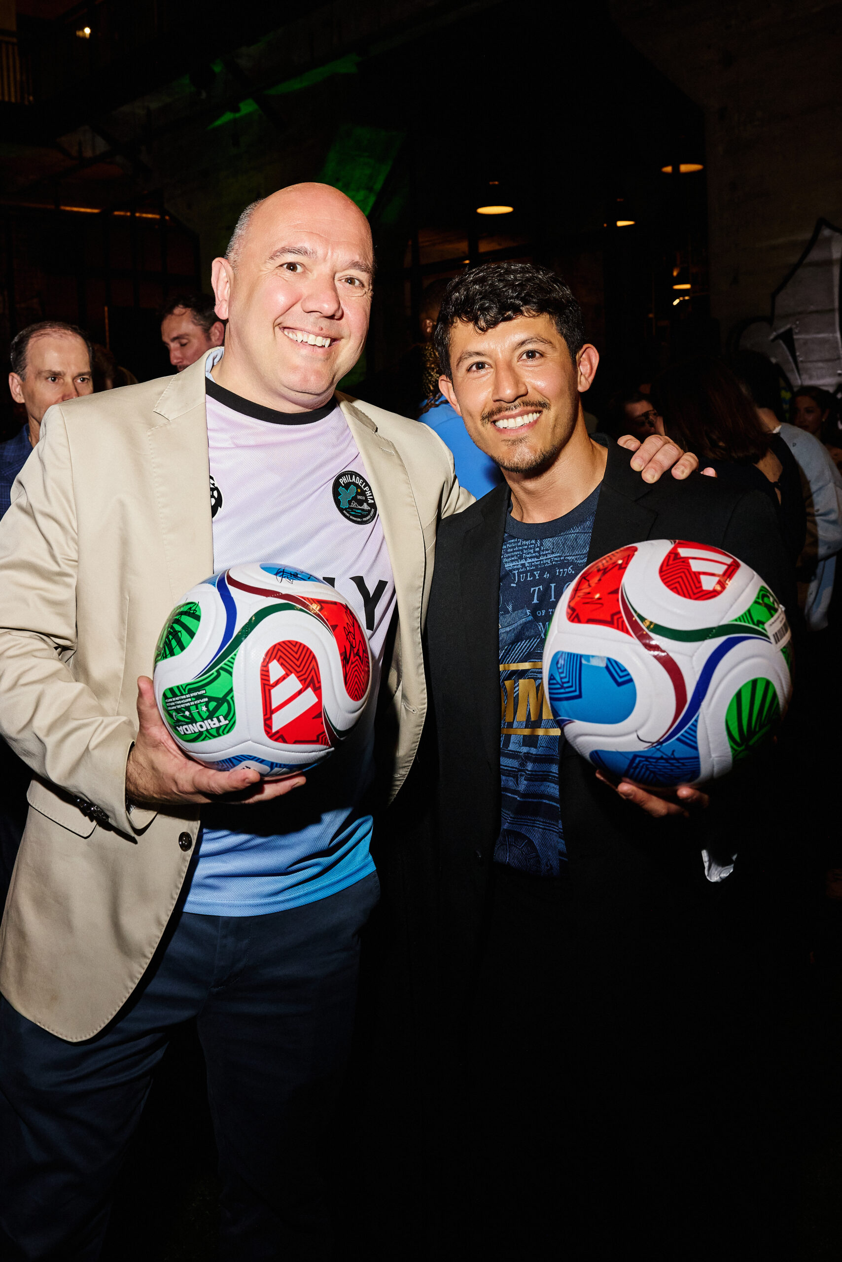 two men posing and holding signed soccer balls