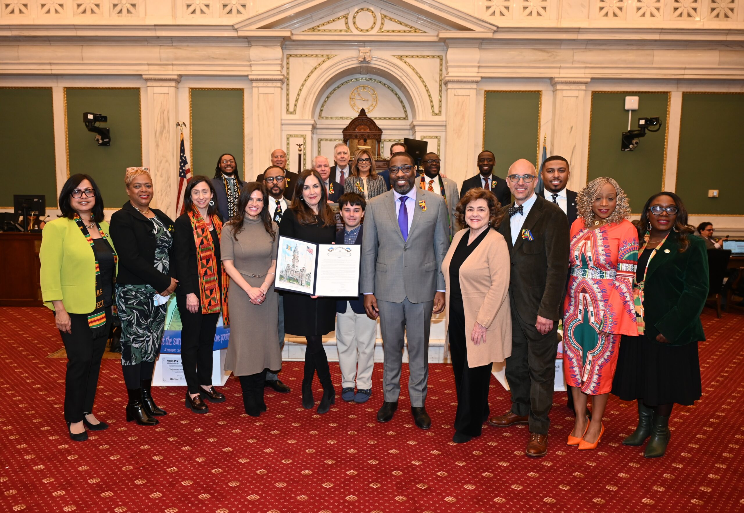 Group of community leaders and guests posing for a photo inside Philadelphia City Hall, with several people holding a framed proclamation.