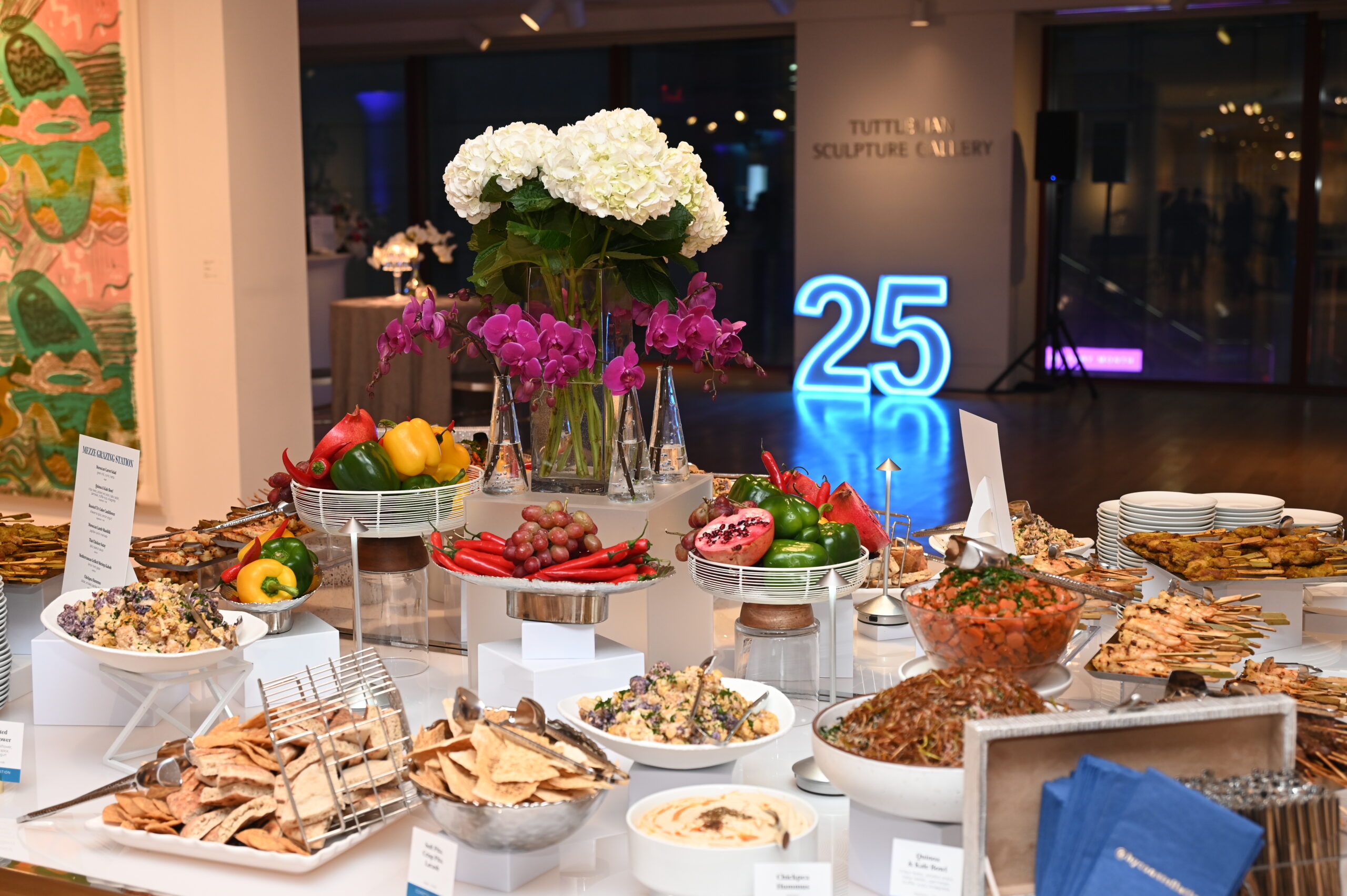 colorful tablescape with a variety of food and florals with illuminated 25 in the background